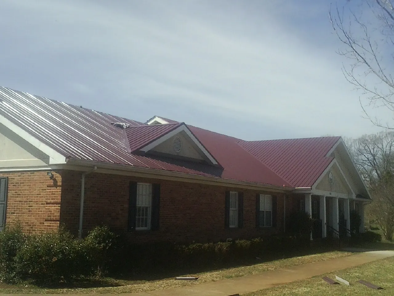 Red metal roof with gabled entries on a long brick building, from a Hail Damage Roof Repair job in Portsmouth
