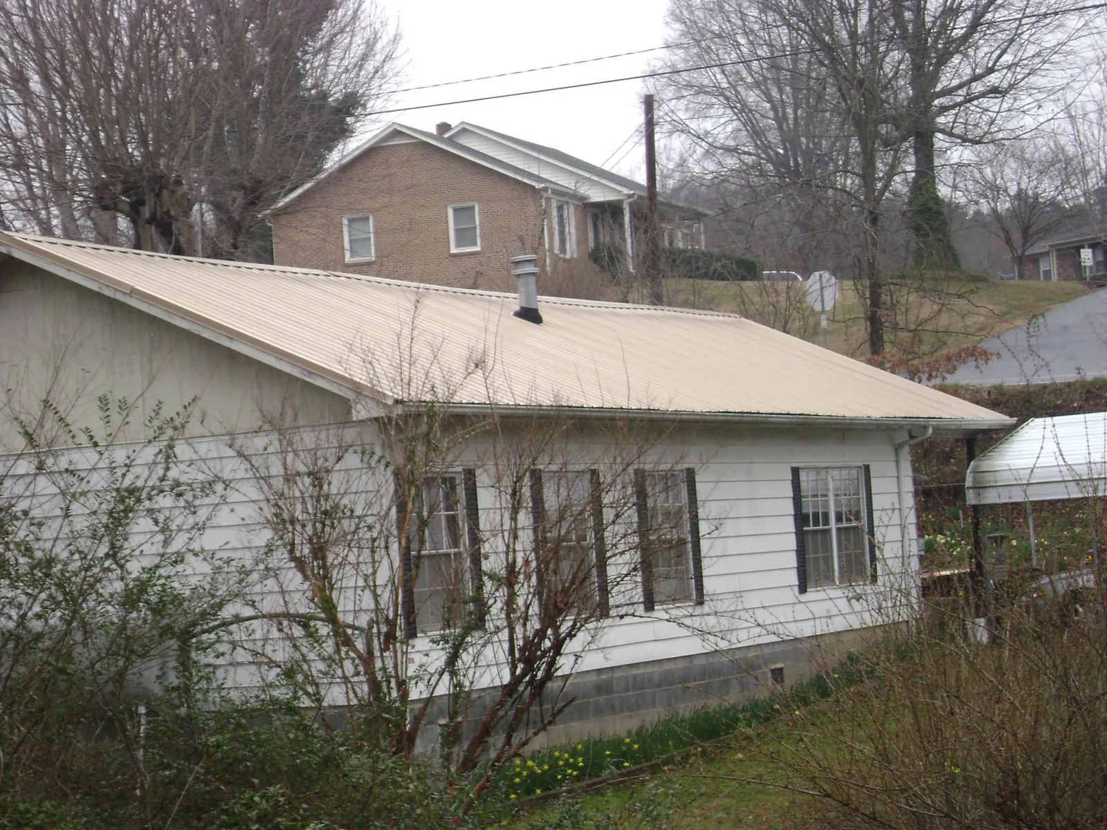 Tan metal roof on a white sided house set into a hillside — Commercial Roofing by Roofing Brothers in Portsmouth